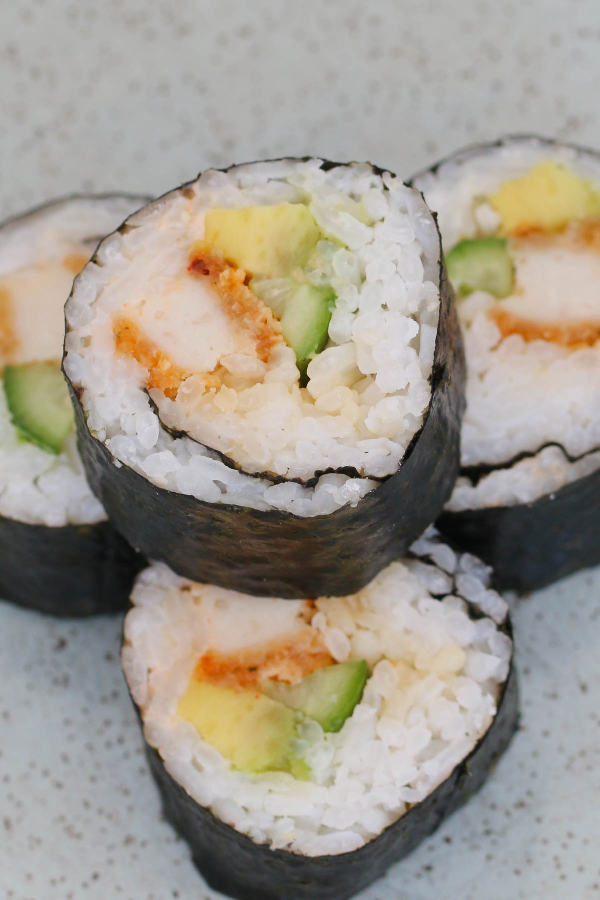 Una pila de sushi con pollo y aguacate en un plato.